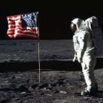 Astronaut looking towards American Flag Standing at the surface of Moon