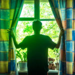 young man opens curtains on the window on the sunny summer morning